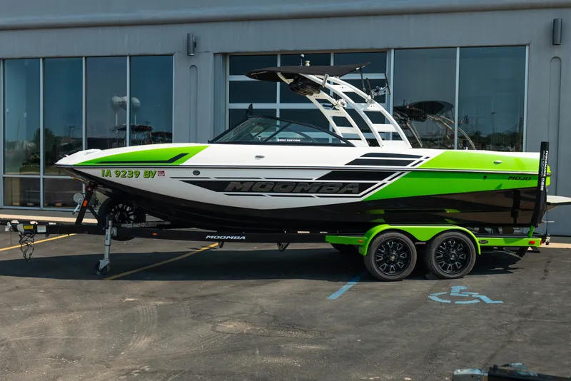 Slide: The Image of 2015 Moomba Mojo boat with green and black design on a trailer, parked outside a building. - 3
