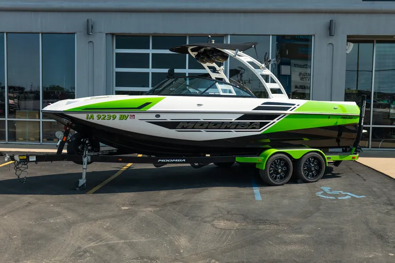 Slide: The Image of 2015 Moomba Mojo boat with green and black design on a trailer, parked outside a building. - 2