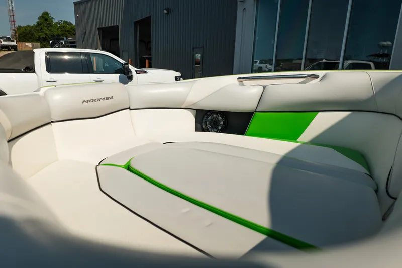 Slide: The Image of 2015 Moomba Mojo boat interior with white and green seating, parked near a building. - 14