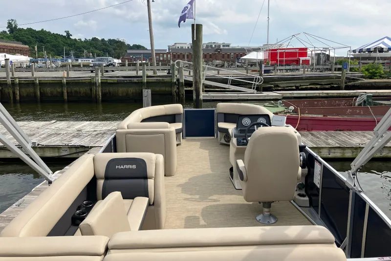 Slide: The Image of 2024 Harris Cruiser 230 pontoon boat docked at a marina, featuring beige seating and modern controls. - 3