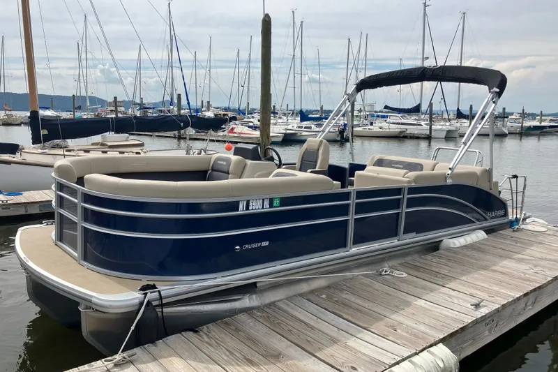 Slide: The Image of 2024 Harris Cruiser 230 pontoon boat docked at marina with sailboats in background. - 1