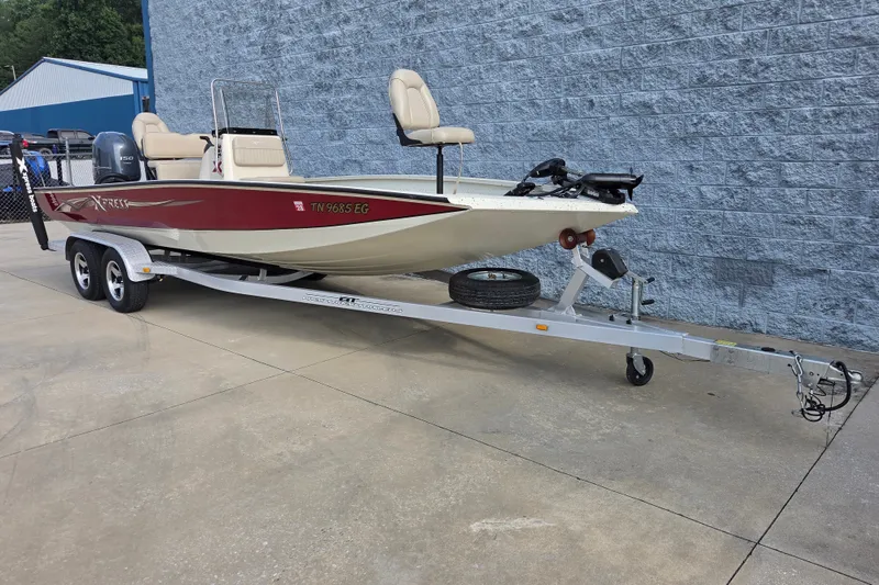 Slide: The Image of 2014 Xpress H22 Bay boat on trailer, parked beside a blue building. - 2