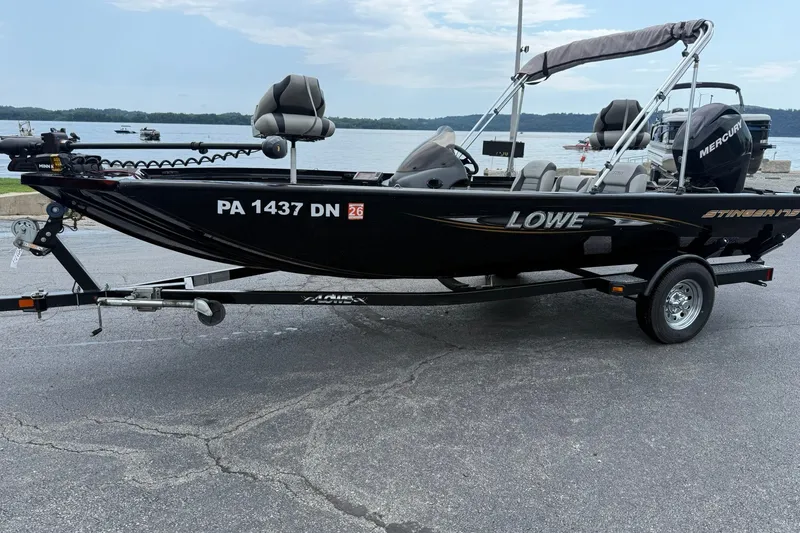 The Image of 2014 Lowe Stinger 175 boat on trailer by a lake, featuring a Mercury engine. - 1