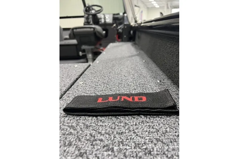 Slide: The Image of Interior view of 2027 Lund 1875 Impact XS boat, featuring carpeted flooring and branded strap. - 14