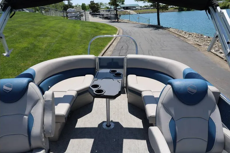 Slide: The Image of 2025 South Bay 220 RS LE 2.75 pontoon boat interior with seating and table by a lake. - 13