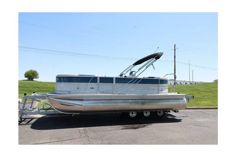 Slide: The Image of 2025 South Bay 220 RS LE 2.75 pontoon boat on trailer, parked outdoors. - 5