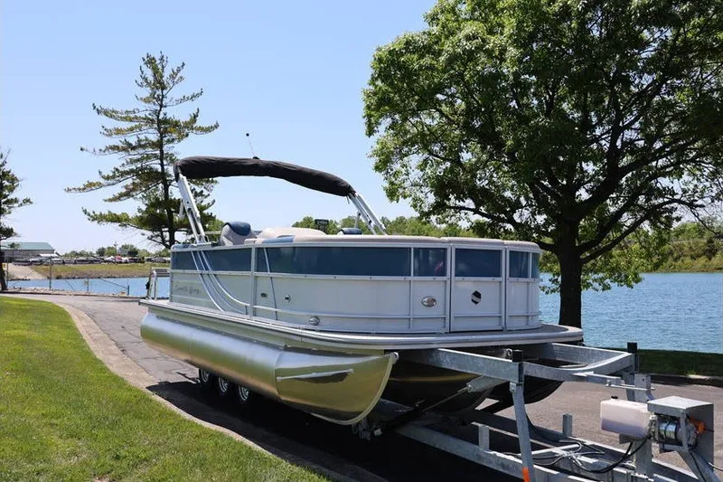 Slide: The Image of 2025 South Bay 220 RS LE 2.75 pontoon boat on trailer by a lake. - 2