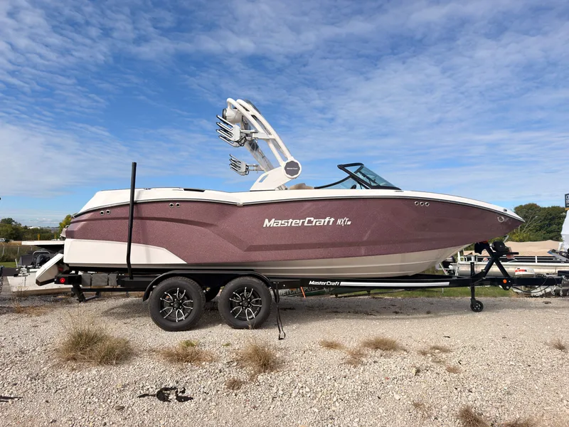 The Image of A 2027 MasterCraft NXT22 boat on a trailer in a gravel lot. - 0