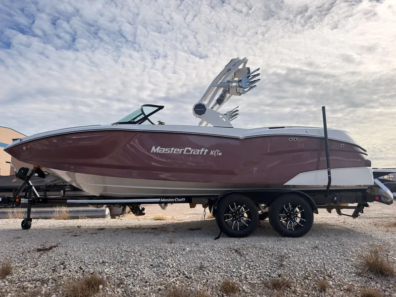 Slide: The Image of A 2027 MasterCraft NXT22 boat on a trailer in a gravel lot. - 5