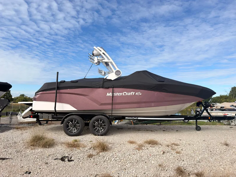 Slide: The Image of A 2027 MasterCraft NXT22 boat on a trailer in a gravel lot. - 1