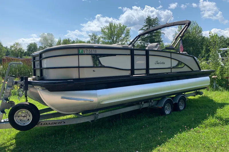 Slide: The Image of 2022 Barletta Lusso 23UC pontoon boat on trailer, parked on grass under a sunny sky. - 1