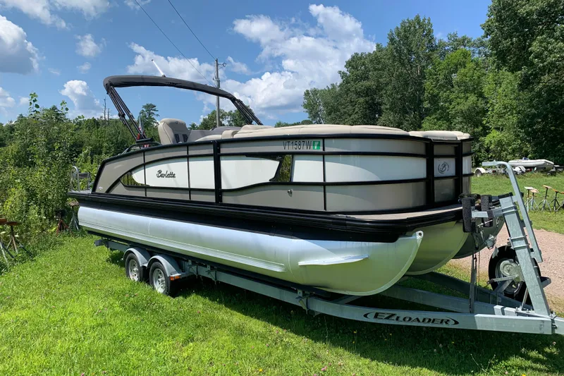 Slide: The Image of 2022 Barletta Lusso 23UC pontoon boat on trailer, parked on grassy area under blue sky. - 0