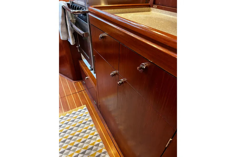 Slide: The Image of Interior of 1999 Oyster 53 Deck Saloon, featuring wooden cabinetry and a compact kitchen area. - 48