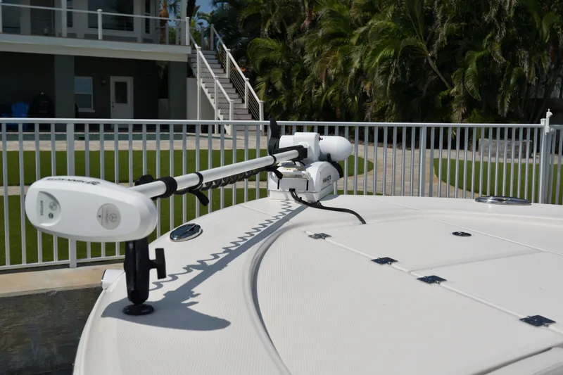 Slide: The Image of 2023 Robalo 246 Cayman boat deck with trolling motor, near a modern house and lush greenery. - 29