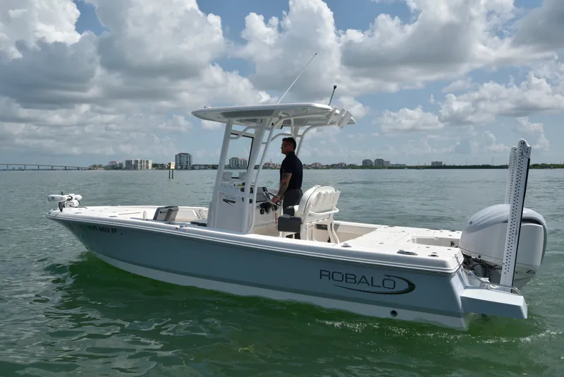 Slide: The Image of A 2023 Robalo 246 Cayman boat on calm water. A man stands at the helm. - 1