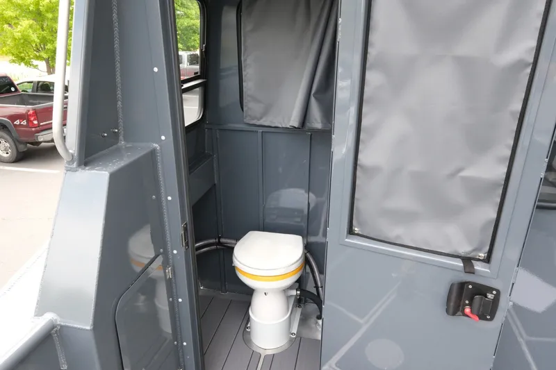 Slide: The Image of 2026 Hewescraft 250 Alaskan boat interior with compact marine toilet and gray paneling. - 17