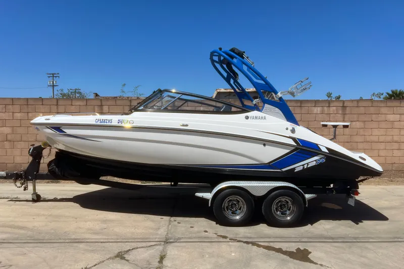 Slide: The Image of 2019 Yamaha Boats 212X on trailer, white and blue design, parked outdoors. - 1