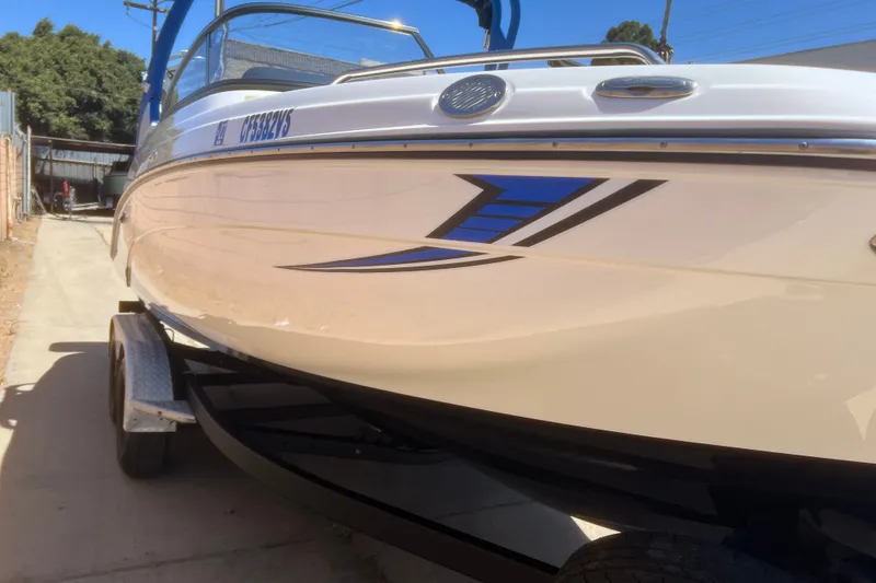 Slide: The Image of 2019 Yamaha Boats 212X on trailer, sleek design with blue accents, parked outdoors. - 18