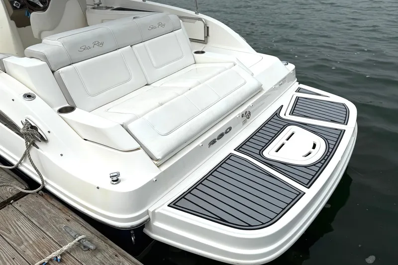 Slide: The Image of 2012 Sea Ray 260 Sundeck boat with white seating and swim platform by the water. - 4