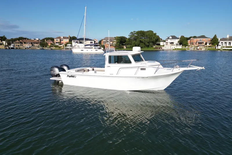 Slide: The Image of 2021 Parker 2520 XLD Sport Cabin boat on calm water near residential shoreline. - 16