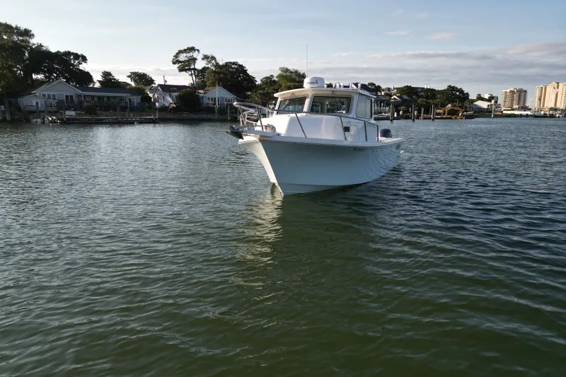 Slide: The Image of 2021 Parker 2520 XLD Sport Cabin boat on calm water near residential shoreline. - 3