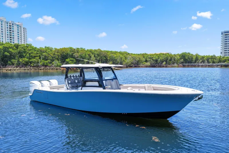 Slide: The Image of 2024 Sportsman Open 352 Center Console boat on calm water, surrounded by greenery and buildings. - 11