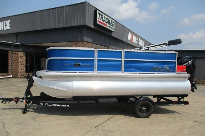 The Image of 2027 Sun Tracker Party Barge 16 DLX pontoon boat on trailer, parked outside dealership. - 1