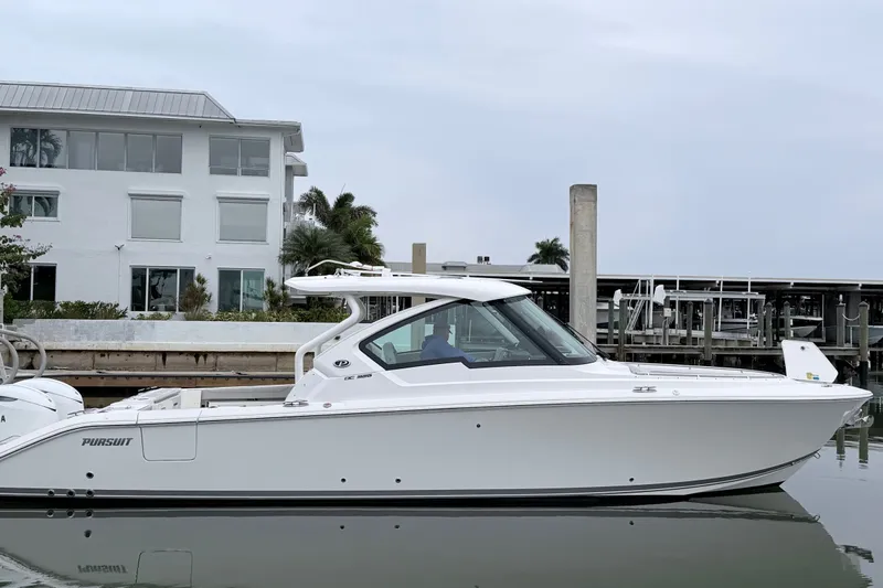 The Image of 2025 Pursuit DC 326 Dual Console boat docked near waterfront building. - 0