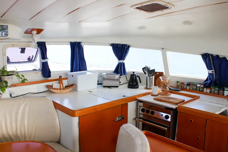 Slide: The Image of Interior of 2001 Lagoon 410 catamaran kitchen with appliances, blue curtains, and wooden cabinetry. - 59