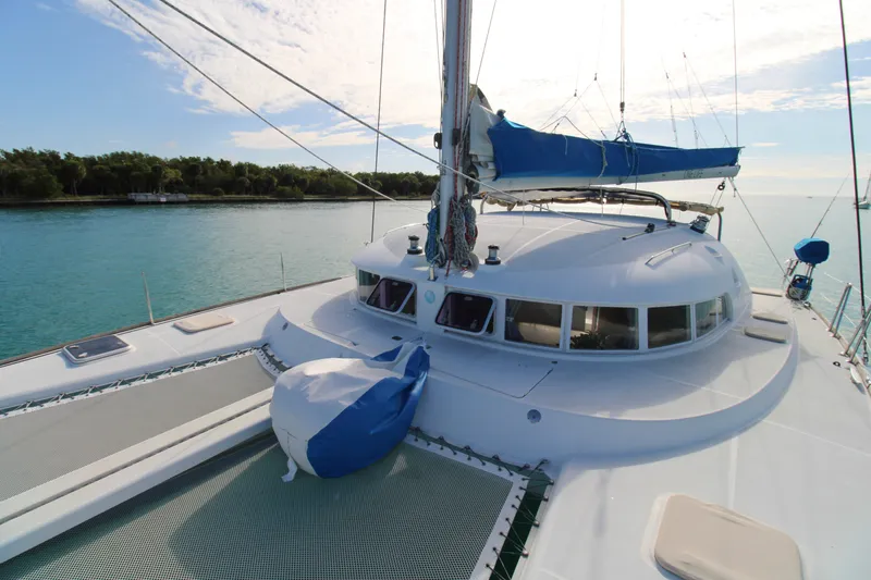 Slide: The Image of 2001 Lagoon 410 catamaran on tranquil water, featuring spacious deck and blue sail cover. - 25
