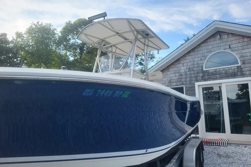 Slide: The Image of 2012 Cobia 217 Center Console boat on trailer, parked near a wooden house. - 4