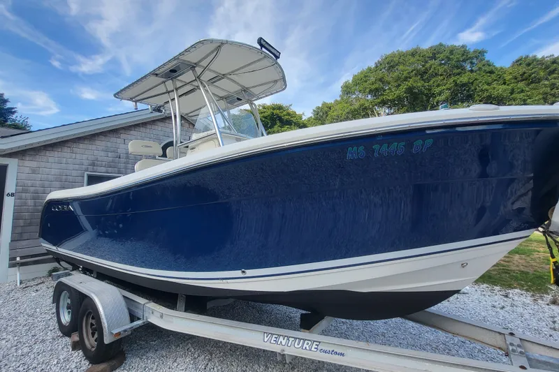 Slide: The Image of 2012 Cobia 217 Center Console boat on trailer, blue hull, parked near a house. - 1