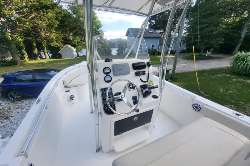 Slide: The Image of 2012 Cobia 217 Center Console boat with steering wheel and control panel, parked near trees. - 14