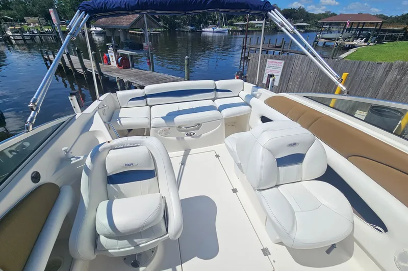 Slide: The Image of 2003 Chaparral 215 SS boat interior with white seating and blue canopy, docked by a serene lake. - 23