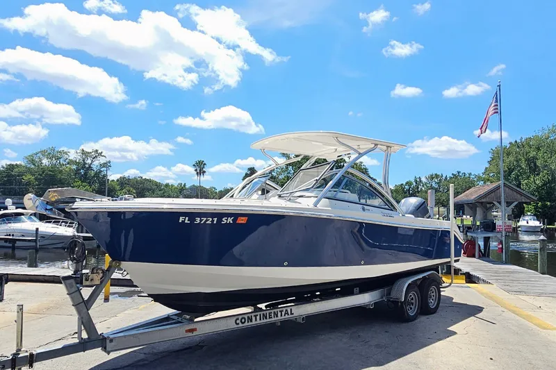 Slide: The Image of 2013 Edgewater 245CX Crossover boat on trailer at marina, under clear blue sky. - 5