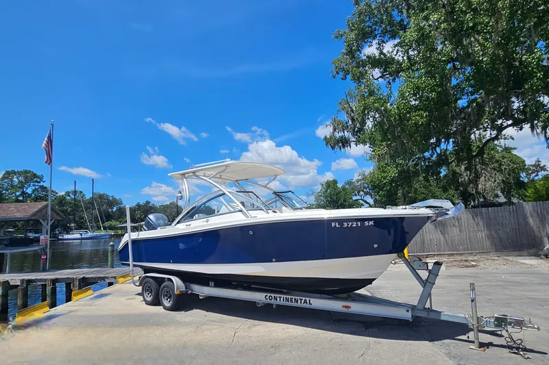 The Image of 2013 Edgewater 245CX Crossover boat on trailer by waterfront, under clear blue sky. - 1