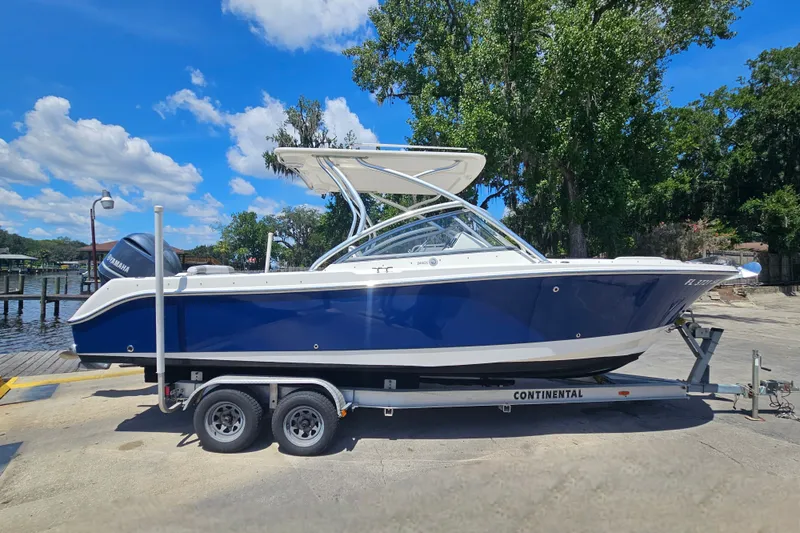 Slide: The Image of 2013 Edgewater 245CX Crossover boat on trailer, blue hull, sunny day, dockside. - 2
