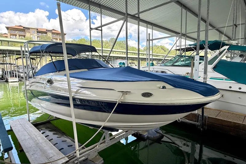 Slide: The Image of 2003 Sea Ray 240 Sundeck boat docked under a covered marina, featuring a blue cover. - 8