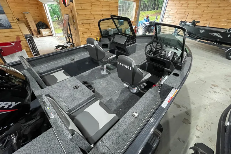 Slide: The Image of 2027 Lund 1700 Adventure Sport boat interior with seating and steering console in a wooden garage. - 14