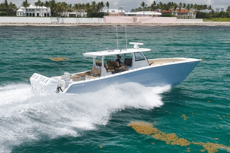Slide: The Image of 2026 Freeman 42LR boat cruising on turquoise ocean near luxury beachfront homes. - 14