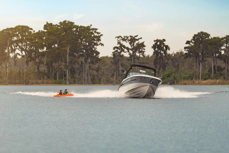 Slide: The Image of A 2027 Sea Ray SDX 270 Surf pulls two people on an inflatable tube across a calm lake. - 22