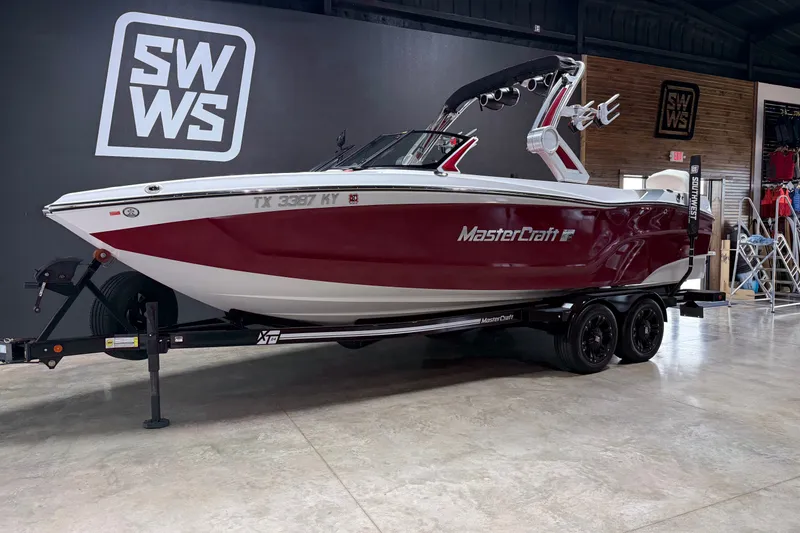 The Image of 2024 MasterCraft XT24 boat on trailer in showroom, featuring sleek red and white design. - 0