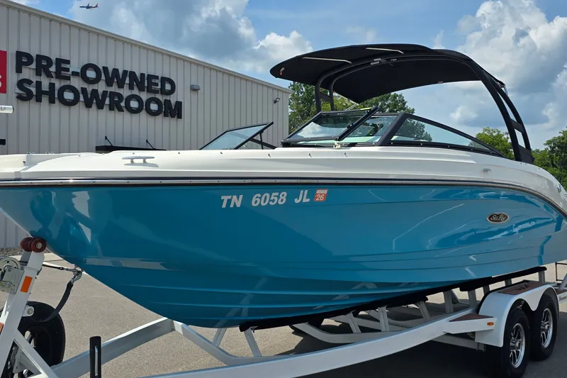 The Image of 2023 Sea Ray SPX 230 boat on trailer at pre-owned showroom, blue hull, sunny day. - 0