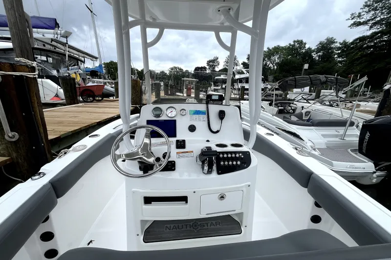 Slide: The Image of 2024 NauticStar 222L Offshore boat dashboard with steering wheel and controls at marina. - 8