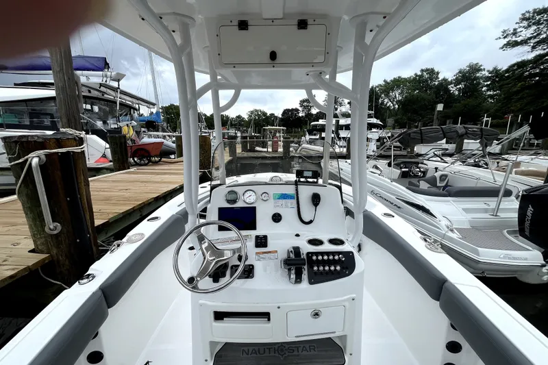 Slide: The Image of 2024 NauticStar 222L Offshore boat dashboard at marina, featuring steering wheel and controls. - 7