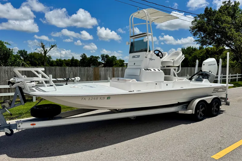 The Image of 2021 SCB R24 boat on trailer, parked on street, under clear blue sky. - 1