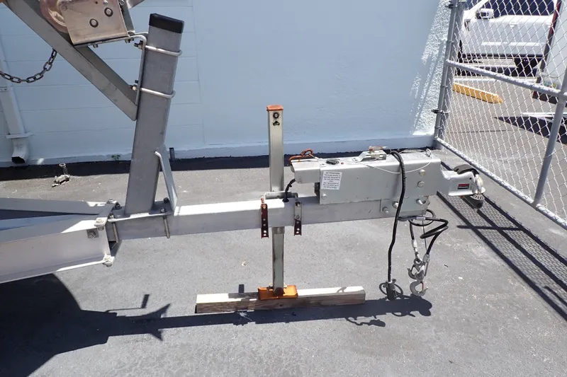 Slide: The Image of Trailer hitch of a 2019 Sailfish 245 DC boat, parked on asphalt near a chain-link fence. - 123