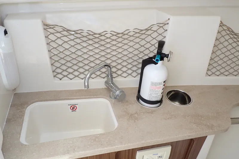 Slide: The Image of 2019 Sailfish 245 DC boat sink area with faucet, fire extinguisher, and storage netting. - 33