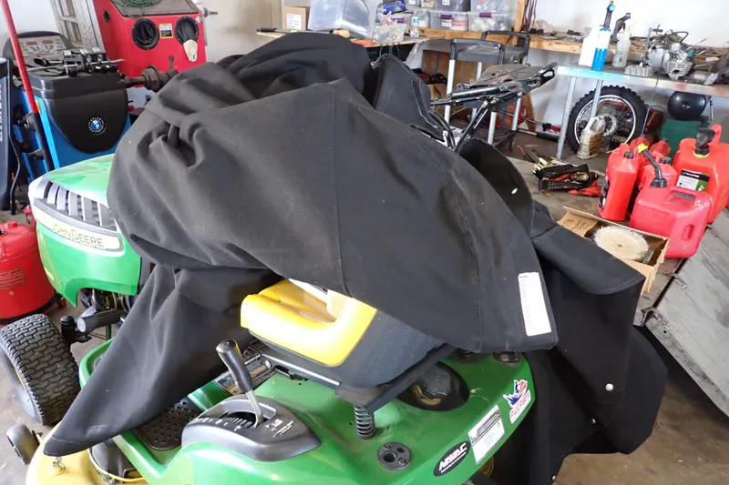 Slide: The Image of A cluttered garage with a covered John Deere lawnmower and various tools. - 134