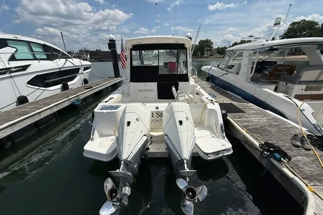 Slide: The Image of 2020 Boston Whaler 325 Conquest docked with twin outboard engines, under a partly cloudy sky. - 6